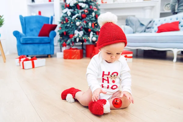 Adorable bébé s'assoit sur le sol et joue avec la boule d'arbre de Noël. Joyeux concept de vacances d'hiver. Noël et Nouvel An . — Photo