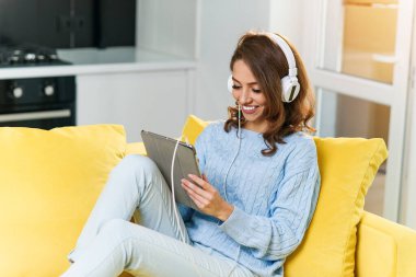 Evdeki kanepede tabletle müzik dinleyen güzel bir kızın portresi..