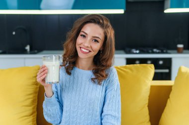 Attractive woman holds a glass of fresh milk and drinks it in the stylish cozy kitchen at the morning. Healthy drinks. clipart