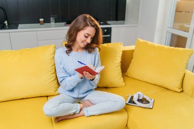 Modern stil mutfağında otururken günlüğüne kişisel notlarını yazan sevimli genç bir kadın..