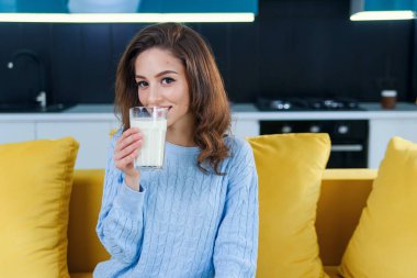Çekici bir kadın bir bardak taze süt tutuyor ve sabahları şık bir mutfakta içiyor. Sağlıklı içecekler.