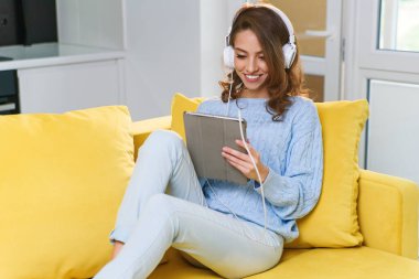 Coberant 30 yaşında, dalgalı kahverengi saçlı, beyaz kulaklık takan, müzik dinleyen, laptopunu ya da tabletini kullanan, rahat evindeki sarı kanepede dinlenen bir kız..
