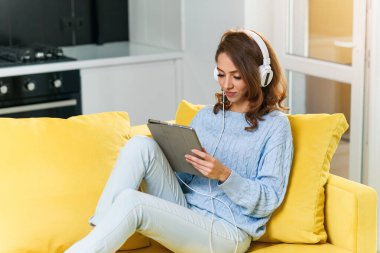 Coberant 30 yaşında, dalgalı kahverengi saçlı, beyaz kulaklık takan, müzik dinleyen, laptopunu ya da tabletini kullanan, rahat evindeki sarı kanepede dinlenen bir kız..