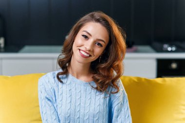 25 yaşında, yumuşak mavi süveterli, gözlüklü güzel bir kız kameraya bakıyor ve şık mutfağın arka planında harika bir gülümseme var..