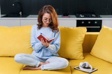 Modern stil mutfağında otururken günlüğüne kişisel notlarını yazan sevimli genç bir kadın..