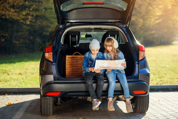 Menino e menina agradável estão olhando para o mapa da estrada enquanto sentado no tronco de automóveis e discutindo a direção do movimento. Viagem de férias em família de carro . — Fotografia de Stock