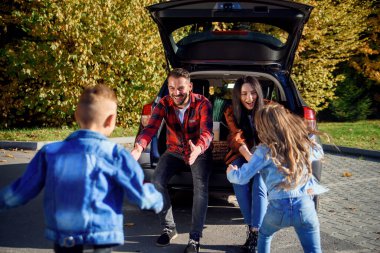 Arabaların bagajında oturan genç ebeveynler mutlu oğullarına ve kızlarına sarılıyorlar..