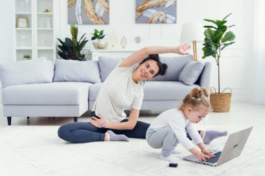 Komik kız laptopla oynarken sportif sağlıklı annesi evde yoga eğitimi alıyor..