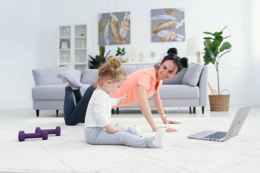 Mutlu anne, küçük kızı evde oynarken yoga pozisyonunda sabah egzersizi yapıyor. Genç sevimli anne meditasyon yaparken eğleniyor. Stresten uzak bir hafta sonu bebeğiyle rahatlıyor..