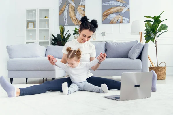 Vrolijke moeder doet ochtendoefeningen in yoga pose terwijl haar dochtertje thuis speelt. jong schattig Moeder having plezier oefenen meditatie ontspannen op stress gratis weekend met baby meisje. — Stockfoto