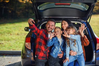 Sevimli çocukları olan mutlu ve şık ebeveynler bagajda otururken akıllı telefondan komik selfie çekiyorlar. Mutlu modern aile kavramı.