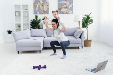Güzel anne ve sevimli küçük kız evde spor yaparken gülümsüyorlar..