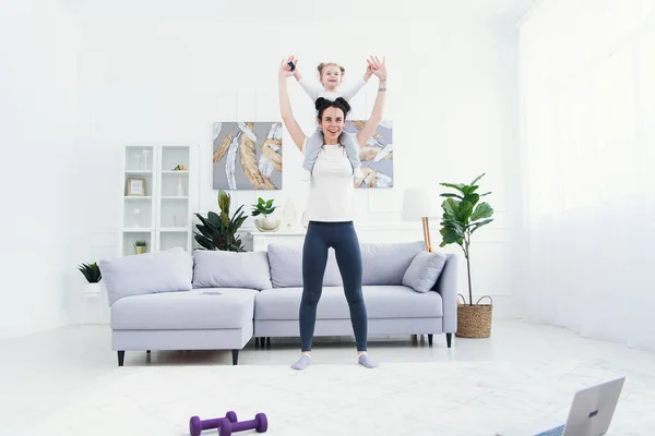 Hermosa mamá y encantadora hijita sonríen mientras hacen ejercicios de fitness juntos en casa . — Foto de Stock