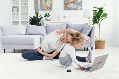 Komik kız laptopla oynarken sportif sağlıklı annesi evde yoga eğitimi alıyor..