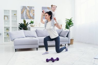 Güzel anne ve sevimli küçük kız evde spor yaparken gülümsüyorlar..