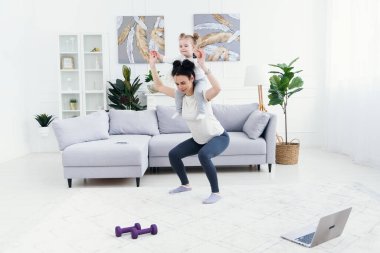 Güzel anne ve sevimli küçük kız evde spor yaparken gülümsüyorlar..