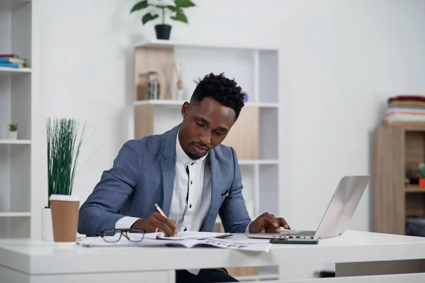 Zakenman met laptop. Jonge Afrikaanse zakenman typt iets op laptop in zijn kantoor.. — Stockfoto