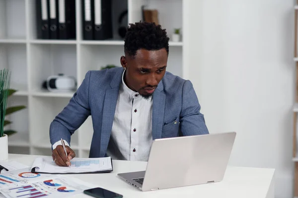 Zakenman met laptop. Jonge Afrikaanse zakenman typt iets op laptop in zijn kantoor.. — Stockfoto