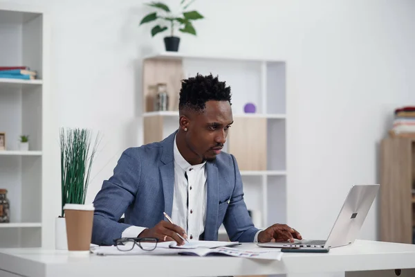 Empresario con laptop. Joven empresario africano está escribiendo algo en el ordenador portátil en su oficina . — Foto de Stock