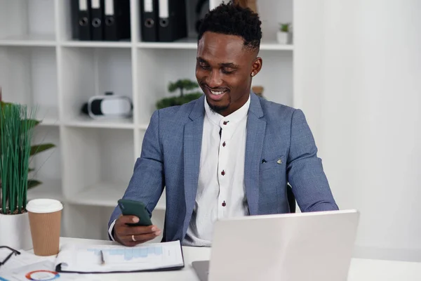 Zwarte zakenman surfen internet pagina 's op de smartphone, met een pauze op het werk in het moderne kantoor. — Stockfoto