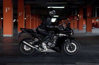 Deri ceketli, uzun saçlı bir kız yeraltı otoparkında motosikletli.