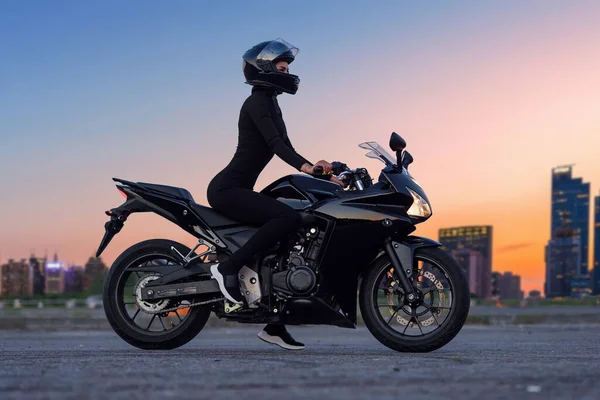 Uma bela menina motociclista apoiando-se em sua superbike fora de um edifício . — Fotografia de Stock