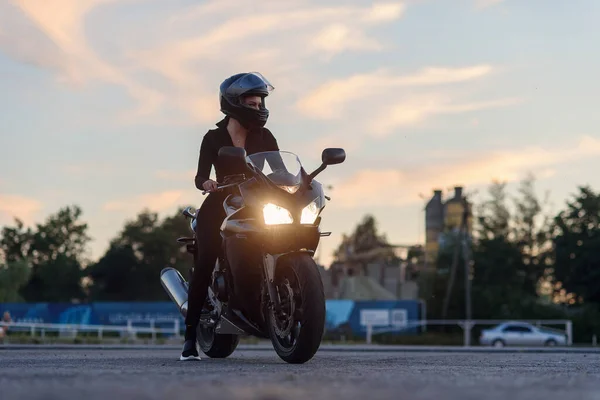 Uma bela menina motociclista apoiando-se em sua superbike fora de um edifício . — Fotografia de Stock