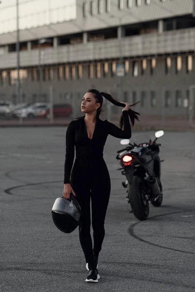 Una hermosa chica motociclista sosteniendo el casco al lado de la superbicicleta fuera de un edificio . — Foto de Stock