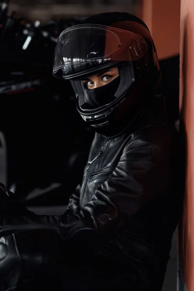 Horizontal shot of unrecognizable woman motorcycle rider driving her enduro motobike or chopper dressed in stylish leather clothes and protective equipment, blurred ligths and cars in background — Stock Photo, Image