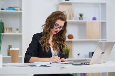 Ofisteki güzel iş kadını şık kıyafetler giyiyor, modern rahat ofisinde otururken kağıda bazı notlar yazıyor..