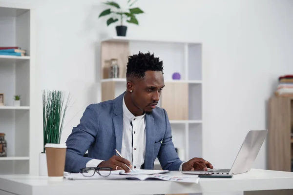 Zakenman met laptop. Jonge Afrikaanse zakenman typt iets op laptop in zijn kantoor.. — Stockfoto