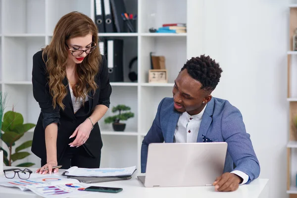 Två olika affärsmän chattar sitter bakom laptop i ämbetet. Spännande kaukasisk kvinna dela idéer eller start affärsplan med svart manlig medarbetare. Informellt samtal, koncept för arbetspauser — Stockfoto