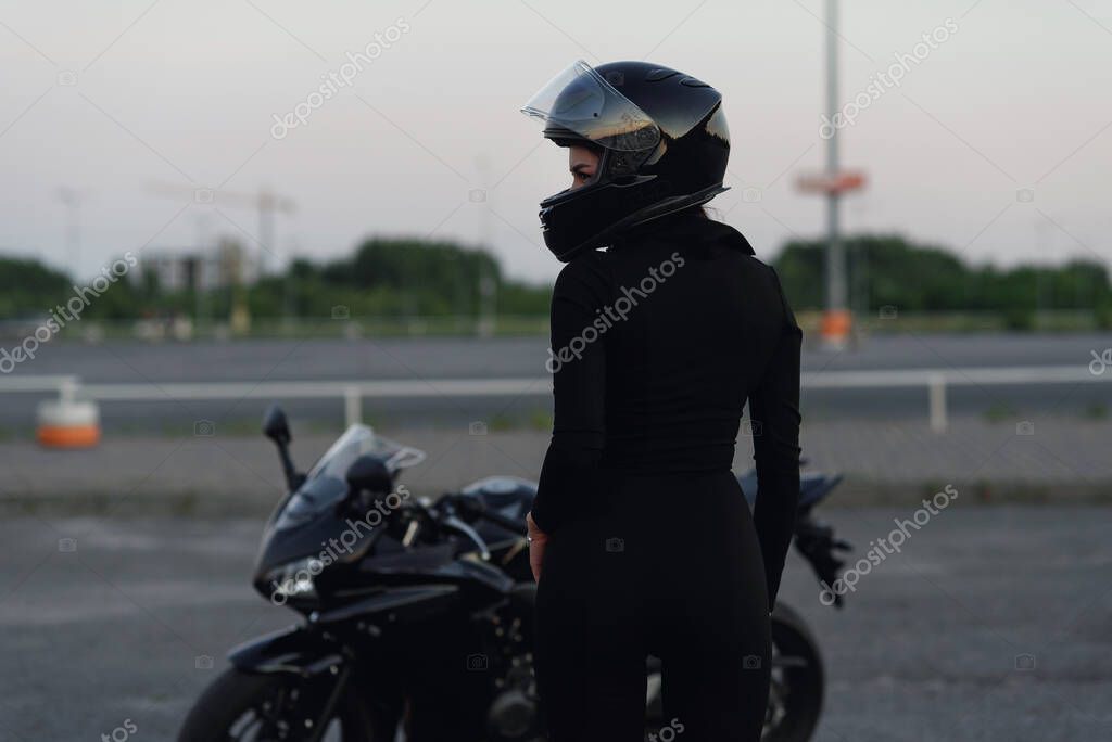 Mujer motorista en chaqueta de cuero negro y casco completo se sienta cerca de la motocicleta