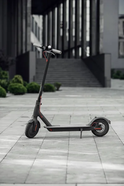 Niza scooter eléctrico negro está aparcado cerca de un gran edificio de vidrio con oficinas . — Foto de Stock