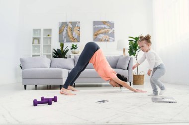 Genç, sevimli anne, gerinme egzersizleri yapıyor ve küçük kızıyla evde yoga yapıyor. Sağlık ve spor konsepti.