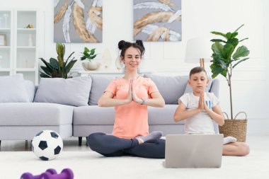 Anne ve oğlu evde dizüstü bilgisayarla yoga yapıyor. Anne ve çocuk sabah egzersiz yapıyor. Sağlıklı yaşam tarzı kavramı.