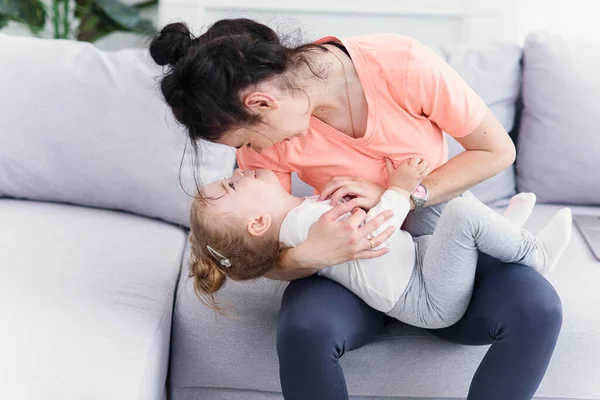 Jovem bela mãe amorosa se divertindo com sua filha criança no sofá em casa aconchegante. Conceito de família feliz . — Fotografia de Stock
