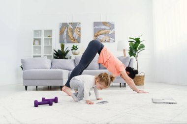 Genç anne esneme egzersizleri yapıyor ve küçük kızıyla evde yoga yapıyor. Sağlık ve spor konsepti.