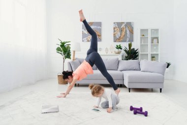 Genç anne esneme egzersizleri yapıyor ve küçük kızıyla evde yoga yapıyor. Sağlık ve spor konsepti.