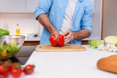 Beyaz adam, İspanyol kırmızı biberini ev mutfağındaki ahşap bir tahtanın üzerinde bıçakla kesiyor..