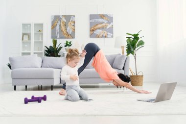 Genç, sevimli anne, gerinme egzersizleri yapıyor ve küçük kızıyla evde yoga yapıyor. Sağlık ve spor konsepti.