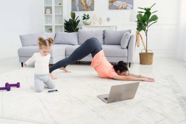 Genç anne esneme egzersizleri yapıyor ve küçük kızıyla evde yoga yapıyor. Sağlık ve spor konsepti.