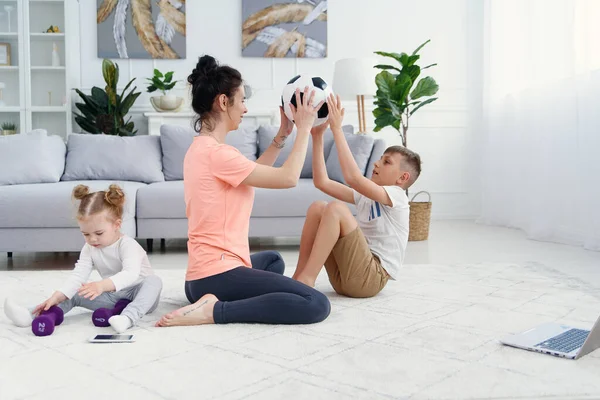 Mãe atlética com filho fazendo exercícios matinais em casa. Mãe e filho fazendo exercícios para o estômago juntos. — Fotografia de Stock