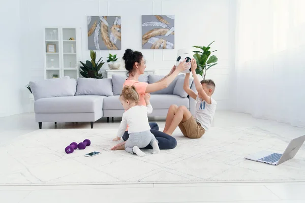 Jovem mãe esportiva com seus filhos fazendo exercícios de treino matinal em casa aconchegante. Conceito de estilo de vida familiar saudável. — Fotografia de Stock