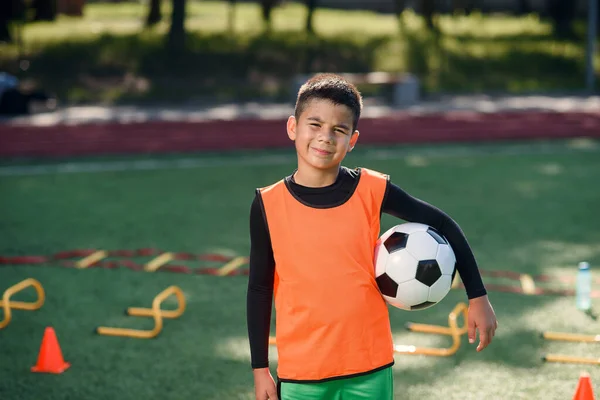 Menino adolescente feliz em uniforme de futebol detém uma bola após o treinamento da manhã no estádio no parque verde urbano. — Fotografia de Stock