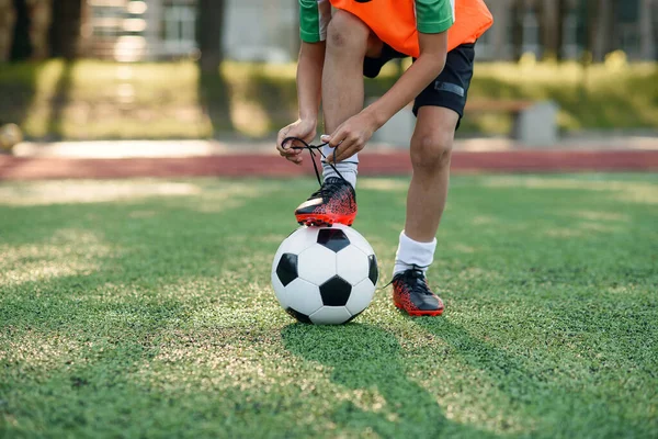 Zamknij buta piłkarza, który stawia nogę na piłkę i wiązania sznurowadła na stadionie piłkarskim na treningu. — Zdjęcie stockowe