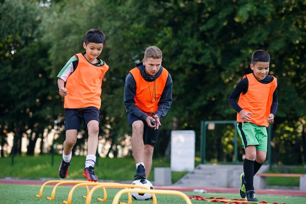 I calciatori adolescenti attivi si allenano insieme sul campo di calcio artificiale e seguono le istruzioni di un allenatore professionista.. — Foto Stock