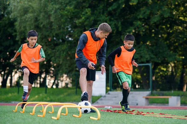 I calciatori adolescenti attivi si allenano insieme sul campo di calcio artificiale e seguono le istruzioni di un allenatore professionista.. — Foto Stock