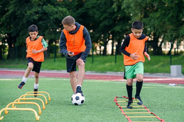 Actieve tiener voetballers trainen samen op kunstmatig voetbalveld en volgen de instructies van een professionele coach. — Stockfoto