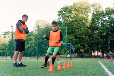 Stadyumdaki futbol antrenmanı sırasında plastikler arasında koşan turuncu yelekli 13 'lü çocuklar motive oldular..